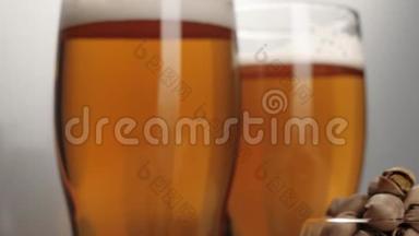 新鲜啤酒。 两个玻璃杯，放着美味的冷啤酒，靠近茶托，在白色背景的木桌上放一些开心果